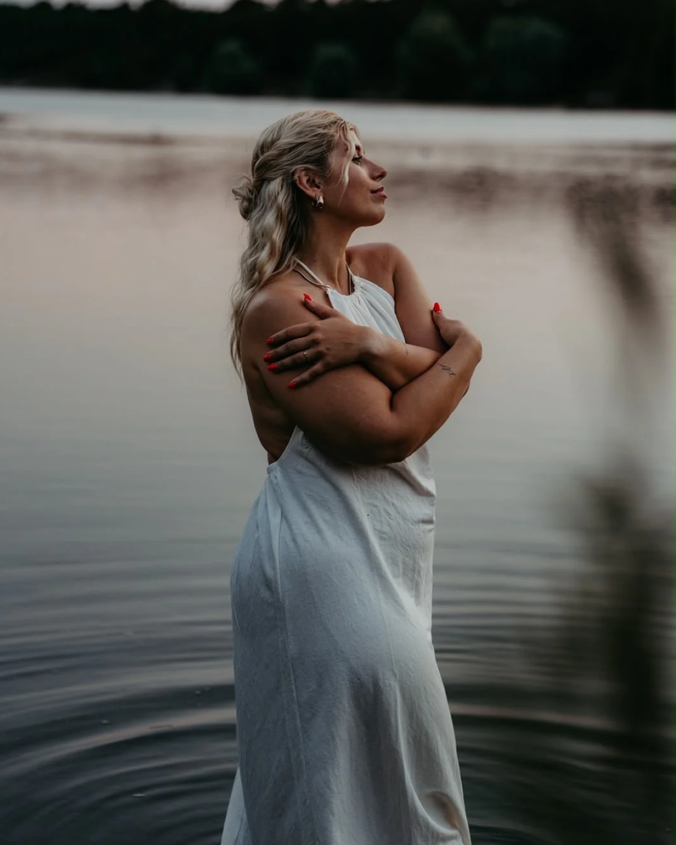 Nathalie trägt ein weißes langes Kleid und steht in einem See.